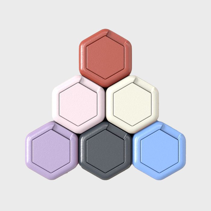 Hexagonal tiles stack in a pyramid formation, displaying muted colorsâ€”red, cream, pink, blue, purple, and grayâ€”against a plain gray background.