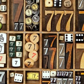 Various items display the number seven, arranged in a wooden grid; includes dice, tiles, discs, and blocks of different textures and colors.