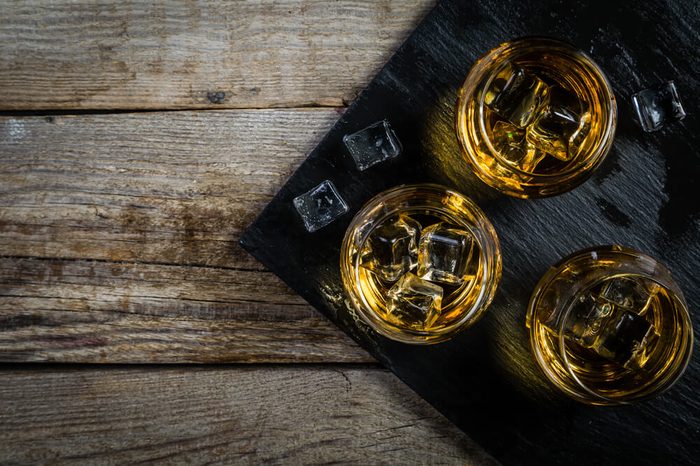 Whiskey with ice in glasses, rustic wood background, copy space