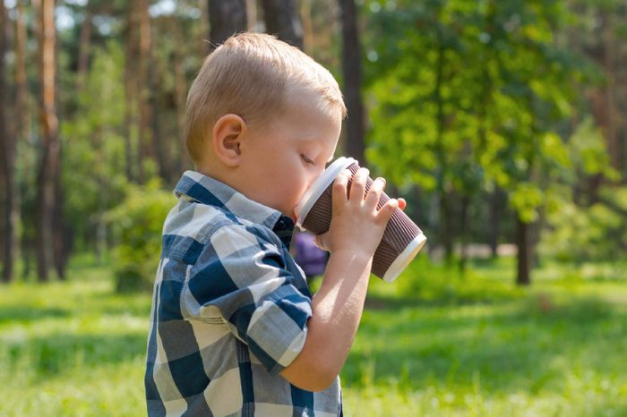 A little boy drinking from a plastic cup in the park on a sunny summer day