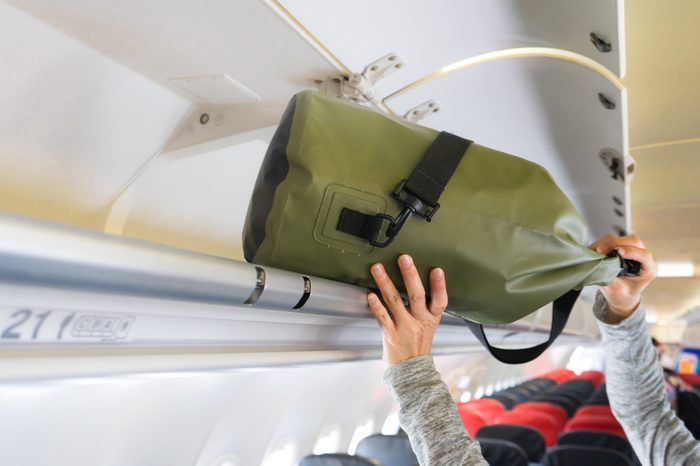 Passenger woman putting luggage into overhead locker on airplane (Selective focus)
