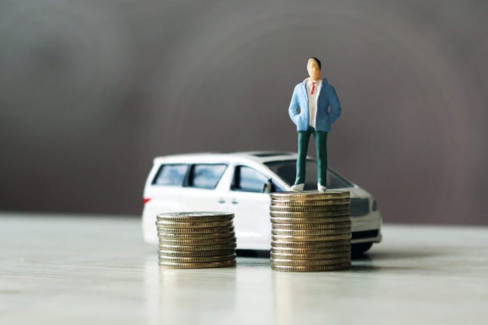 miniature people. The man standing on top of the coins and the car behind them.