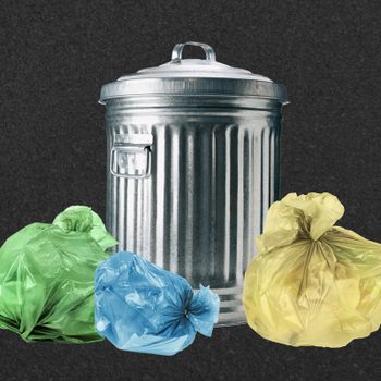 A metal garbage can stands with closed lid, surrounded by green, blue, and yellow tied plastic bags, against a plain dark background.