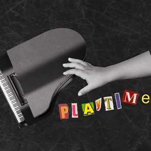 A hand reaches over a grand piano keyboard, with colorful cutout letters spelling 