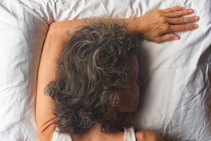 High angle close up view of middle aged woman sleeping face down on pillow with arm overhead (selective focus)