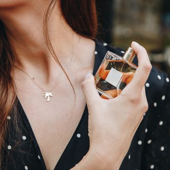 young woman wearing black and white polka dot dress posing with a bottle of expensive perfume. beautiful and stylish european fashion blogger posing with perfume outdoors. perfect summer outfit.