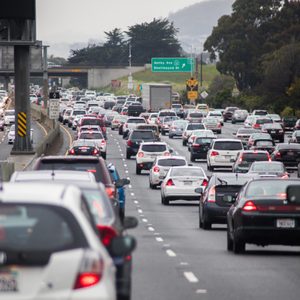 Cars are congested on a multi-lane highway near a green exit sign for Ashby Ave. Trees line the road.