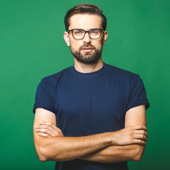 A person wearing glasses stands confidently with arms crossed, set against a plain green background.