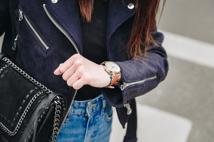fashion blogger holding a trendy black purse and checking the time on her elegant watch. young stylish woman wearing a suede leather jacket, ripped jeans and black ankle boots.