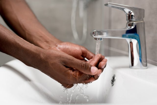 Hands being washed under running water in a white sink, with a shiny metal faucet in a bathroom setting.