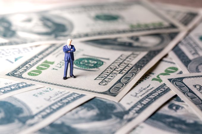Miniature figurine toys standing on dollar with money and work concept. Focus on the businessman.