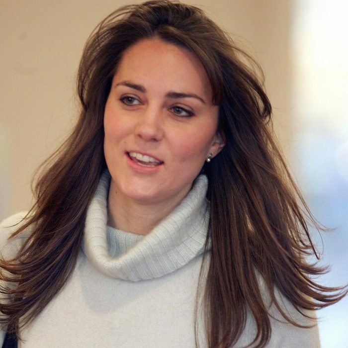 Woman walking indoors, wearing a light turtleneck sweater, hair flowing, with soft lighting in the background.
