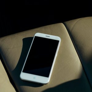 A smartphone rests motionless on beige car seat, partially bathed in sunlight.
