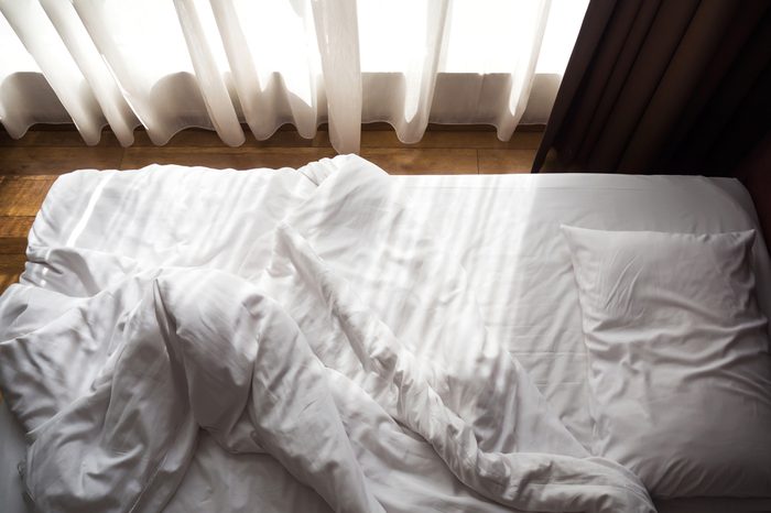 Messy bed. White pillow and blanket with sunlight through window. Relaxing concept. Unmade bed.