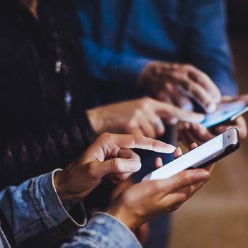 Hands tap smartphone screens in dim lighting, focusing on interacting with devices.