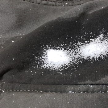 White powder scattered, resting on dark fabric, creating a noticeable contrast in a close-up view.