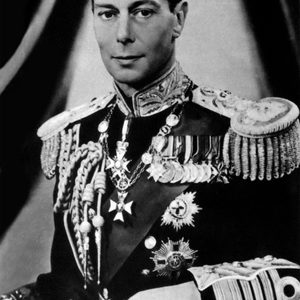 A man wearing a decorated military uniform sits against a draped fabric background, adorned with medals and ornate epaulettes.