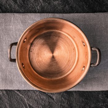 Copper pot rests quietly on a gray fabric, situated on a dark stone surface.