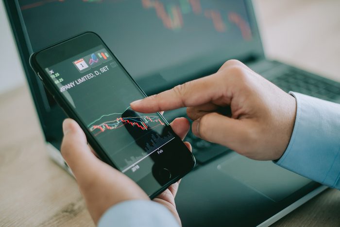Business man point to the smart phone show financial market chart and Blurred background of a laptop show financial market chart, Stock market concept.