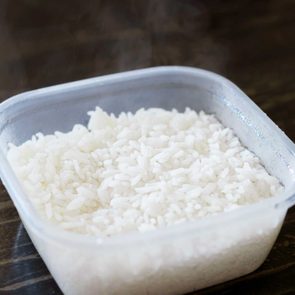 A portion of cooked white rice sits in a clear plastic container on a dark wooden surface.