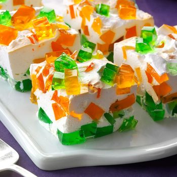 Colorful gelatin squares rest on whipped dessert, served on a white plate, creating a vibrant, layered appearance.