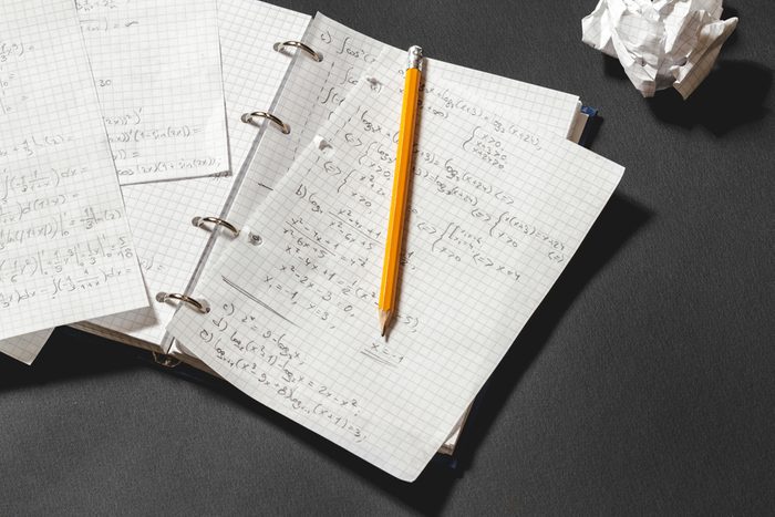 Solving a mathematical problem in a notebook. Crumpled piece of paper on black desk.