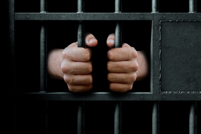 A closeup of a dimly lit prison holding cell door with gripping the bars - 3D render