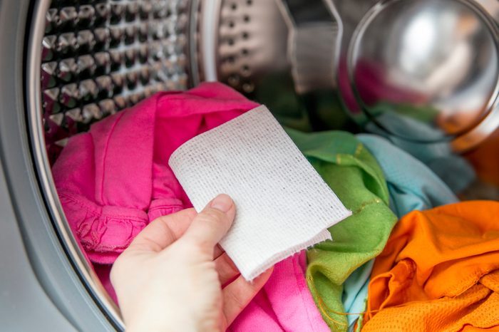 Woman hand put color absorbing sheet inside a washing machine, allows to wash mixed color clothes without ruining colors concept.