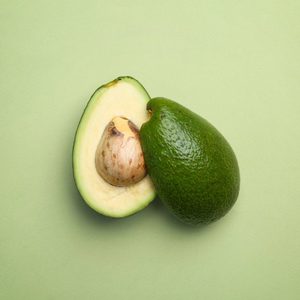 Halved avocado displaying seed, resting on light green surface.