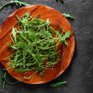 Arugula lies fresh on a wooden platter, surrounded by a dark, textured surface.