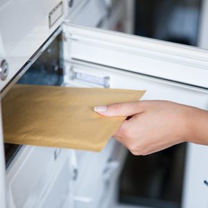 Hand inserts brown envelope into white mail slot in a residential setting.
