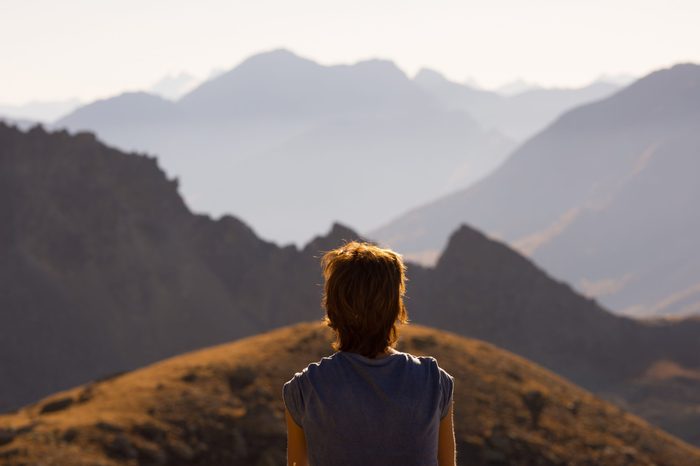 One person looking at view high up on the Alps. Expasive landscape, idyllic view at sunset. Rear view.