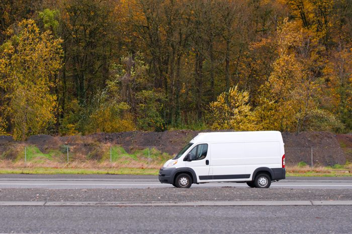 Commercial compact cargo mini van vehicle for small business going on the entrance to interstate road with autumn yellow gold trees on the background
