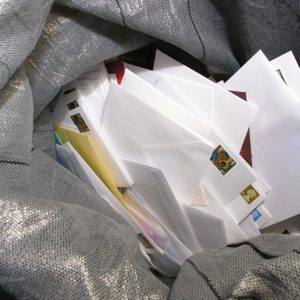 Envelopes rest in an open, gray mail sack, revealing colorful stamps and hidden contents.
