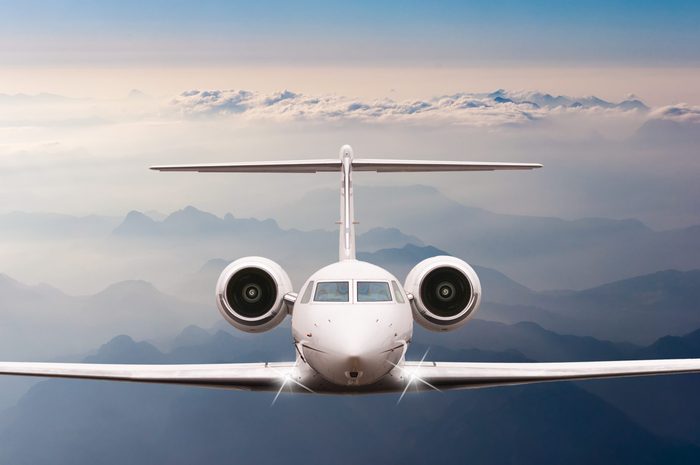 Private Airplane fly over clouds and Alps mountain on sunset. Front view of a big passenger or cargo aircraft, business jet, airline. Transportation, travel concept