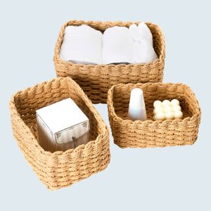 Woven baskets store various items: towels, a box, and bottles. Baskets are rectangular, placed against a light neutral background.