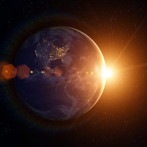 Earth partially illuminated, city lights visible, sun rising; surrounded by stars in space.