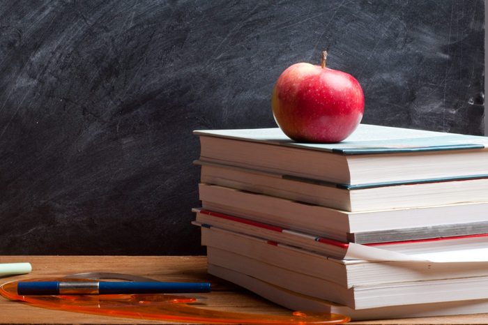 red apple resting on the book with chalk board as background