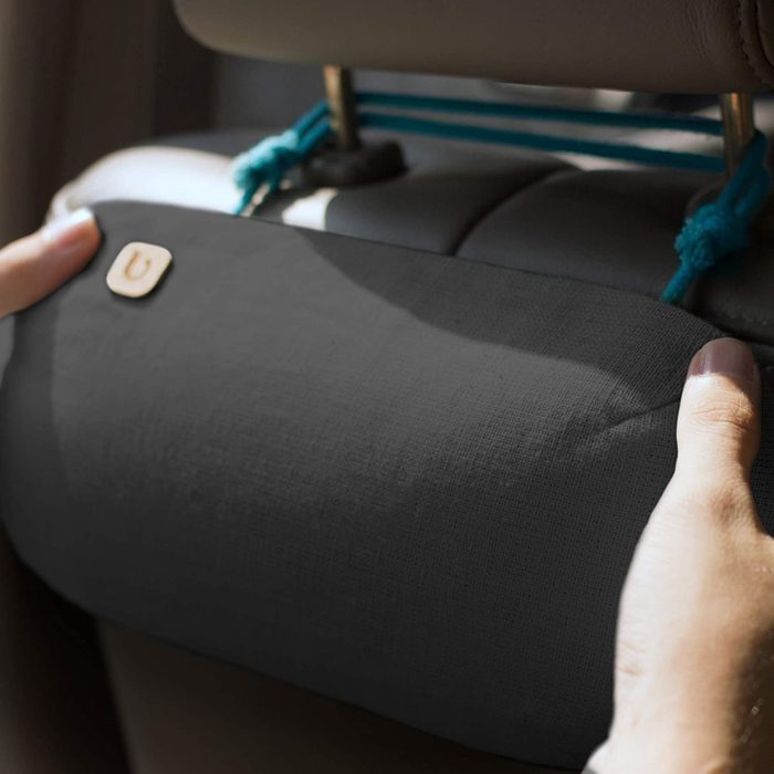 Hands adjust a black cushion attached with blue cords to a car seat headrest, illuminated by sunlight.
