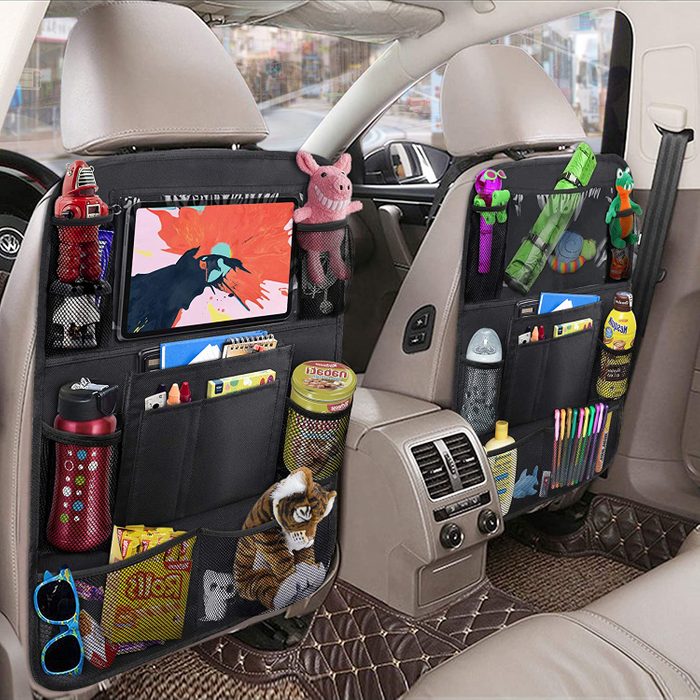 Backseat organizers hold toys, drinks, and tablets in a car interior, with pockets filled with a pig plush, pens, snacks, and colorful items.