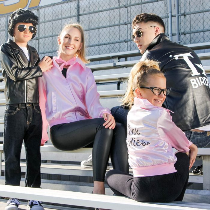 Family sits on bleachers, wearing retro-style jackets. Jackets say 