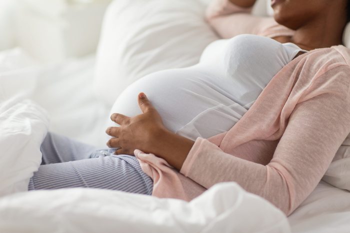 pregnancy, people and rest concept - close up of happy pregnant african american woman lying in bed at home bedroom