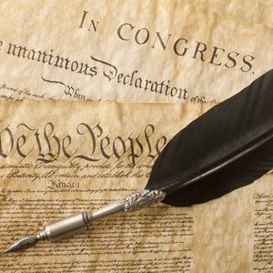 A quill rests on historical documents, featuring text 
