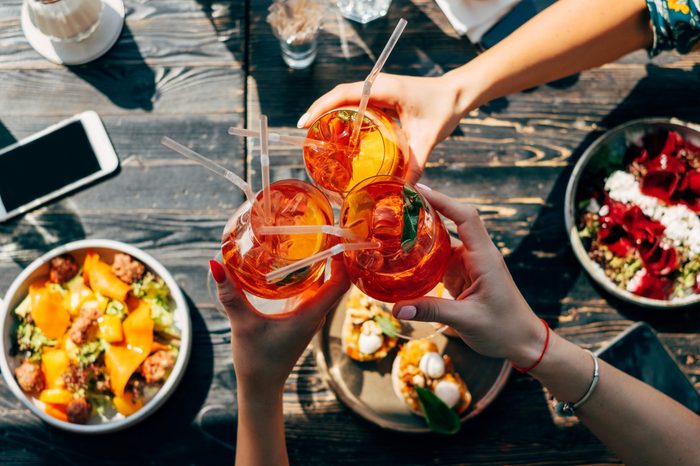 Friends toasting, saying cheers holding tropical aperol spritz cocktails. Top view of dinner table