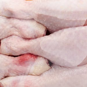 Raw chicken drumsticks packaged closely together in a sealed plastic container. The meat appears fresh with slight pink and white hues.