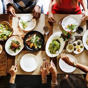 Diners enjoy a meal, sharing various dishes on a wooden table adorned with salads, meats, wine glasses, and vibrant decor.
