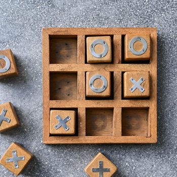 Wooden tic-tac-toe game, X and O blocks, partially placed in grid on textured surface.