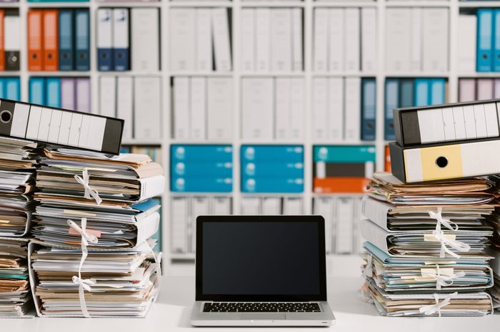 Piles of paperwork in the office and laptop on the desktop