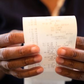 Hands holding a printed receipt, examining its details, in a dimly lit environment.