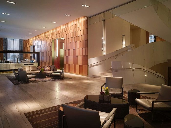 Spiral staircase gracefully ascends in a stylish lobby with modern furniture and warm wooden paneling, creating an inviting atmosphere.